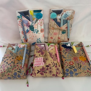 May include: Five gift packages wrapped in floral paper, tied with twine, and containing stationery items. Each package has a pen, a paperclip, and other small items. One package has a sticker that says "Read More Books".