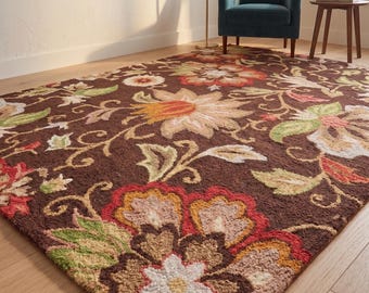 Puede incluir: Una alfombra rectangular con fondo marrón oscuro y un patrón floral a gran escala en tonos rojo, naranja, amarillo, verde y crema. La alfombra tiene una superficie de pelo texturizado y copetudo con intrincados motivos botánicos.