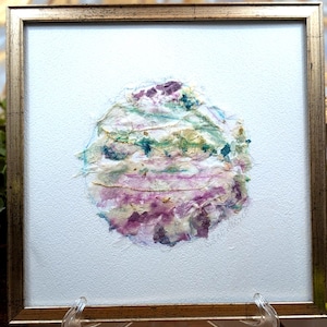 May include: A square framed artwork featuring a circular collage of textured paper in shades of purple, green, and blue, accented with thin gold threads and metallic flecks, set against a plain white background within a metallic gold frame.