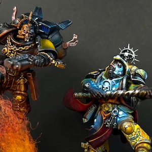 Puede incluir: Dos figuras de guerreros en miniatura muy detalladas. La figura de la izquierda lleva una armadura negra y dorada con un casco de calavera, blandiendo un arma sobre una columna de humo naranja. La derecha tiene armadura azul y amarilla y un bastón.