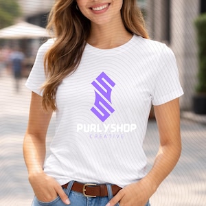 Può includere: T-shirt bianco con un design geometrico viola e la scritta "PURLYSHOP CREATIVE". La maglietta ha girocollo e maniche corte. La modella indossa jeans blu e una cintura marrone.