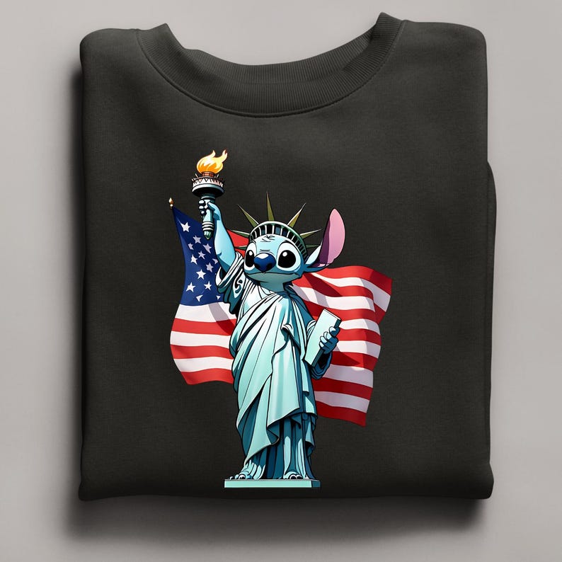 Puede incluir: Sudadera negra con un personaje de dibujos animados como la Estatua de la Libertad, sosteniendo una antorcha y una tableta, con una bandera estadounidense de fondo. El personaje es azul con ojos grandes y una oreja distintiva. La antorcha tiene una llama amarilla.