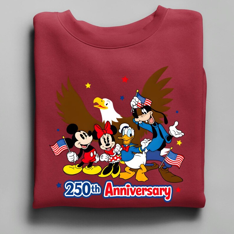 Puede incluir: Sudadera granate con Mickey Mouse, Minnie Mouse, Donald Duck y Goofy con banderas americanas y un &aacute;guila. El texto "250th Anniversary" se muestra en una pancarta roja y azul.