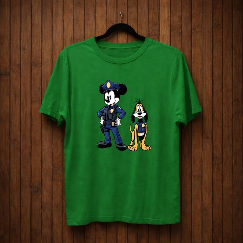 May include: Green t-shirt featuring a cartoon illustration of Mickey Mouse and Pluto dressed as police officers. Mickey Mouse is in a blue uniform with a police hat, and Pluto is in a yellow uniform.