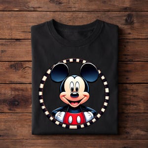May include: Black t-shirt featuring a colorful graphic of Mickey Mouse. The cartoon character is smiling, wearing red shorts and white gloves, and framed by a black and white striped circle. The shirt is folded on a wooden surface.