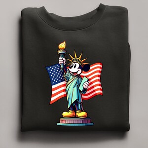 Puede incluir: Sudadera negra con una representaci&oacute;n de dibujos animados de Mickey Mouse como la Estatua de la Libertad, sosteniendo una antorcha y una tableta, con una bandera estadounidense de fondo. El dise&ntilde;o es colorido y patri&oacute;tico.