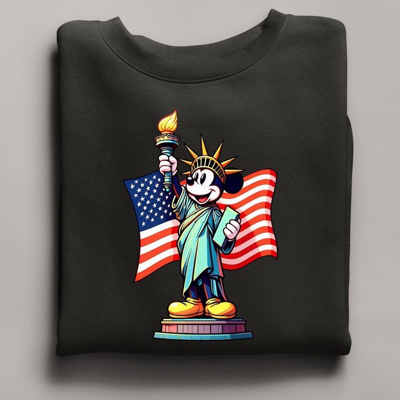 Puede incluir: Sudadera negra con una representaci&oacute;n de dibujos animados de Mickey Mouse como la Estatua de la Libertad, sosteniendo una antorcha y una tableta, con una bandera estadounidense de fondo. El dise&ntilde;o es colorido y patri&oacute;tico.