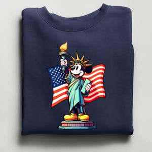 Puede incluir: Sudadera azul marino con una representaci&oacute;n de dibujos animados de Mickey Mouse como la Estatua de la Libertad, sosteniendo una antorcha y una tableta. La bandera estadounidense est&aacute; en el fondo. El dise&ntilde;o es colorido y patri&oacute;tico.