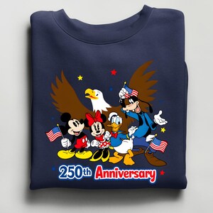 Puede incluir: Sudadera azul marino con una ilustraci&oacute;n de Mickey, Minnie, Donald y Goofy sosteniendo banderas americanas, con un &aacute;guila calva. El texto "250th Anniversary" es rojo y blanco.