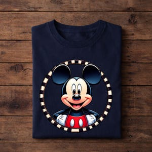 May include: Navy blue t-shirt featuring a colorful illustration of Mickey Mouse inside a black and white striped circle. Mickey Mouse is wearing a red shirt with white buttons and white gloves. The shirt is folded on a wooden surface.