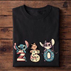 Puede incluir: Camiseta negra con los personajes Stitch, Lilo y Angel sosteniendo los n&uacute;meros 2, 5 y 0. Los n&uacute;meros est&aacute;n decorados con estrellas y colores patri&oacute;ticos. La camiseta est&aacute; hecha de un material suave.