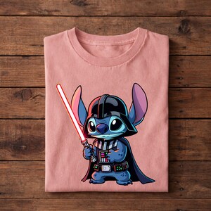 Pu&ograve; includere: Una maglietta rosa chiaro con un personaggio dei cartoni animati, Stitch, vestito da Darth Vader. Stitch &egrave; blu con grandi orecchie, indossa un casco e un mantello neri e tiene una spada laser rossa. Il disegno &egrave; centrato sulla maglietta.