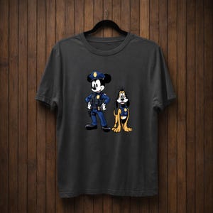 May include: Dark gray t-shirt featuring a cartoon illustration of Mickey Mouse and Pluto dressed as police officers. Mickey Mouse is in a blue police uniform with a hat, and Pluto is wearing a police vest. The design is centered on the shirt.