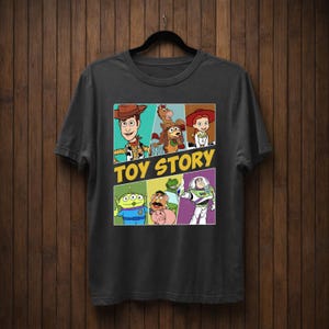 K&ouml;nnte beinhalten: Dunkelgraues T-Shirt mit einer farbenfrohen Grafik von Charakteren aus dem Animationsfilm "Toy Story". Das Design zeigt Woody, Buzz Lightyear und andere Charaktere mit den Worten "TOY STORY" in Gelb.