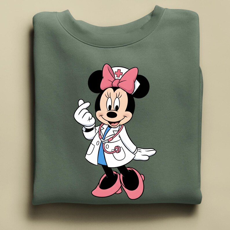 Puede incluir: Sudadera verde con Minnie Mouse de dibujos animados vestida de m&eacute;dico. Minnie Mouse lleva una bata blanca, un lazo rosa y un estetoscopio. Est&aacute; haciendo un coraz&oacute;n con los dedos. La sudadera est&aacute; doblada.