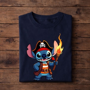 Pode incluir: Camiseta azul marinho com um personagem de desenho animado vestido de pirata. O personagem azul tem olhos grandes, um chap&eacute;u de pirata com uma caveira e ossos cruzados e uma tocha com uma chama. A camiseta est&aacute; dobrada em uma superf&iacute;cie de madeira.