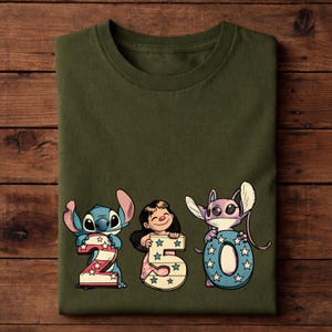 Puede incluir: Camiseta verde oliva con los personajes Stitch, Lilo y Angel sosteniendo los n&uacute;meros 2, 5 y 0. Los n&uacute;meros est&aacute;n decorados con estrellas y rayas. La camiseta est&aacute; doblada sobre una superficie de madera.