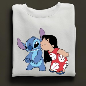 Peut inclure: Sweat-shirt blanc avec un dessin de Stitch, un extraterrestre bleu, embrass&eacute; par une fille en robe rouge. Le motif repr&eacute;sente les personnages du film d'animation Lilo & Stitch. Le sweat-shirt est un v&ecirc;tement confortable et d&eacute;contract&eacute;.