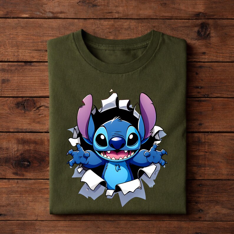 May include: Olive green t-shirt featuring a graphic of the character Stitch bursting through a torn hole. Stitch is blue with large ears, a wide smile, and outstretched arms. The design is centered on the folded shirt.