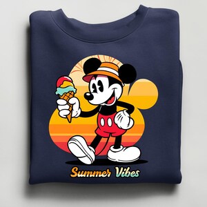 May include: Navy blue sweatshirt featuring a cartoon Mickey Mouse holding an ice cream cone. Mickey is wearing red shorts, white gloves, and a hat. The background has a sunset design with the words "Summer Vibes".
