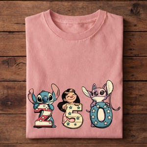 Puede incluir: Una camiseta rosa claro con los personajes Stitch, Lilo y Angel sosteniendo los n&uacute;meros 2, 5 y 0. Los n&uacute;meros est&aacute;n decorados con estrellas y rayas. La camiseta est&aacute; hecha de un material suave.