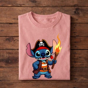 Pode incluir: Camiseta rosa claro com um personagem de desenho animado pirata segurando uma tocha. O personagem &eacute; azul, usando um chap&eacute;u de pirata preto com uma caveira, uma bandana vermelha e um colete marrom. A tocha tem uma chama laranja brilhante.