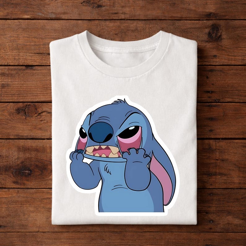 May include: White t-shirt featuring a cartoon image of Stitch from Lilo & Stitch. The blue alien character is depicted with an angry expression, holding his mouth with his hands. The design is a sticker-like graphic.