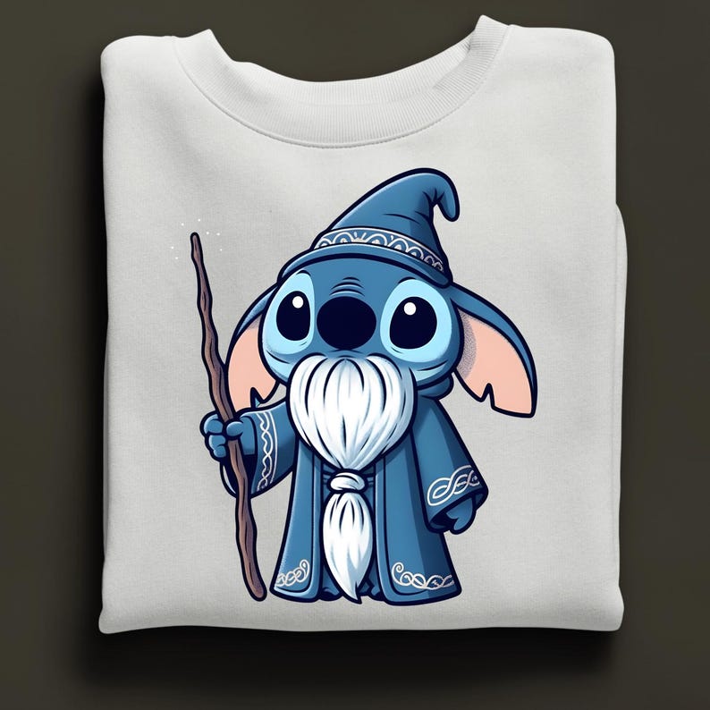 Puede incluir: Sudadera blanca con un personaje de dibujos animados vestido de mago. El personaje es azul con ojos grandes, lleva un sombrero y una t&uacute;nica de mago azules y sostiene un bast&oacute;n de madera. Tema de fantas&iacute;a.