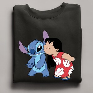 Peut inclure: Sweat-shirt noir avec une illustration de Stitch et Lilo du film Lilo & Stitch. Lilo, en robe rouge, embrasse Stitch. Stitch est bleu avec de grandes oreilles. Le design est une repr&eacute;sentation des personnages Disney.
