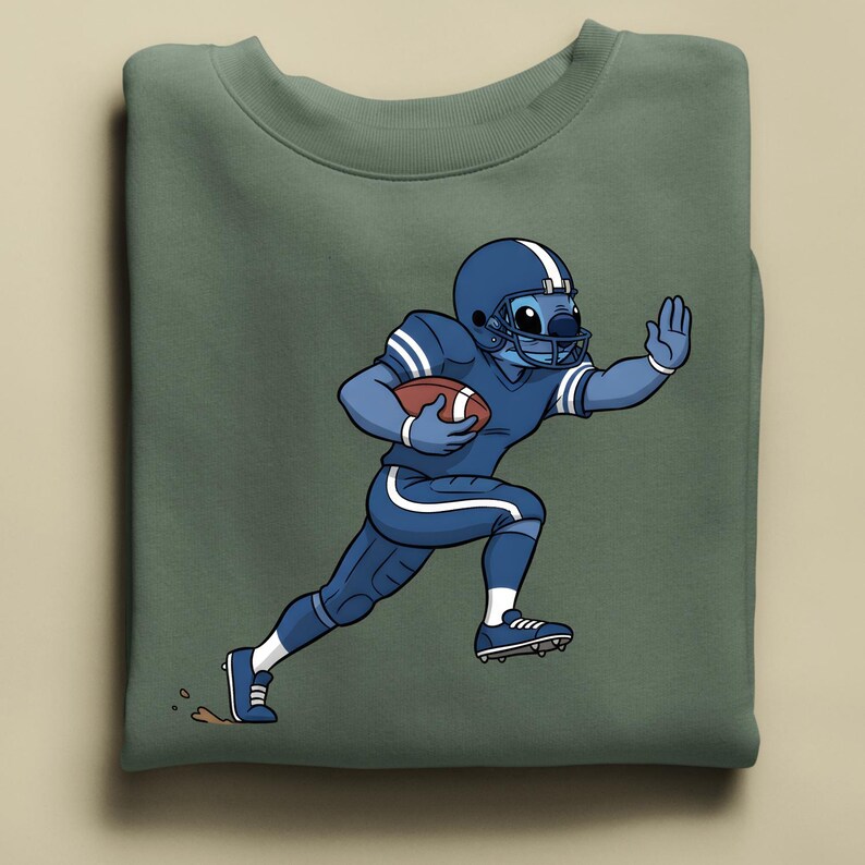May include: A sage green sweatshirt with a cartoon character in a blue American football uniform, helmet, and holding a football. The character is running, with one hand raised. The design has white stripes and accents.