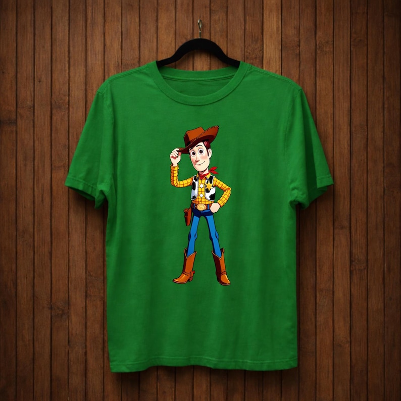 May include: A green t-shirt with a cartoon cowboy character illustration. The character wears a brown cowboy hat, yellow vest, red neckerchief, blue jeans, and brown boots. The t-shirt is displayed on a black hanger.