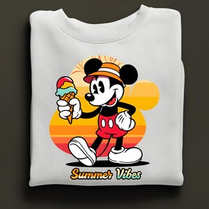 May include: White sweatshirt featuring a cartoon Mickey Mouse holding an ice cream cone. Mickey is wearing a hat and red shorts. The background has a sunset design with the words "Summer Vibes".