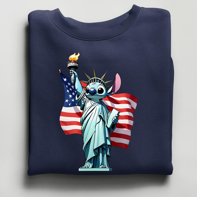 Puede incluir: Sudadera azul marino con un personaje de dibujos animados como la Estatua de la Libertad, sosteniendo una antorcha y una bandera estadounidense. El personaje es azul claro con ojos grandes y una oreja rosa. La bandera tiene rayas rojas y blancas y estrellas azules.