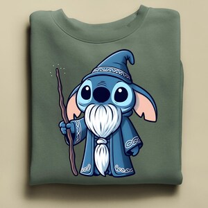 Puede incluir: Sudadera verde oliva con un personaje de dibujos animados de mago. El mago tiene piel azul, ojos grandes y una barba blanca. Lleva una t&uacute;nica y un sombrero azules, sosteniendo un bast&oacute;n de madera. El dise&ntilde;o est&aacute; centrado en la parte delantera.