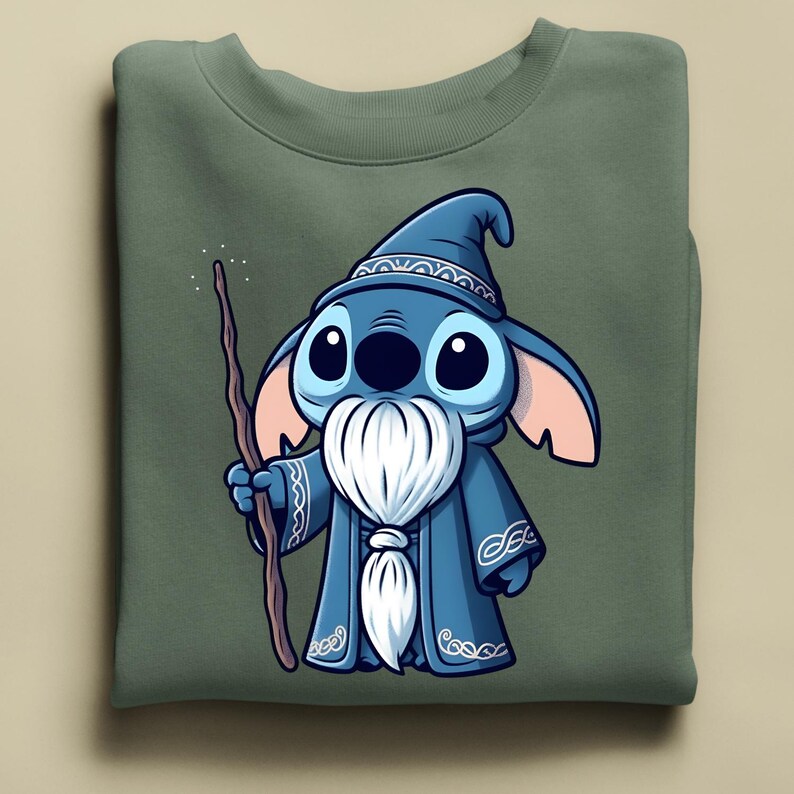 Puede incluir: Sudadera verde oliva con un personaje de dibujos animados de mago. El mago tiene piel azul, ojos grandes y una barba blanca. Lleva una t&uacute;nica y un sombrero azules, sosteniendo un bast&oacute;n de madera. El dise&ntilde;o est&aacute; centrado en la parte delantera.