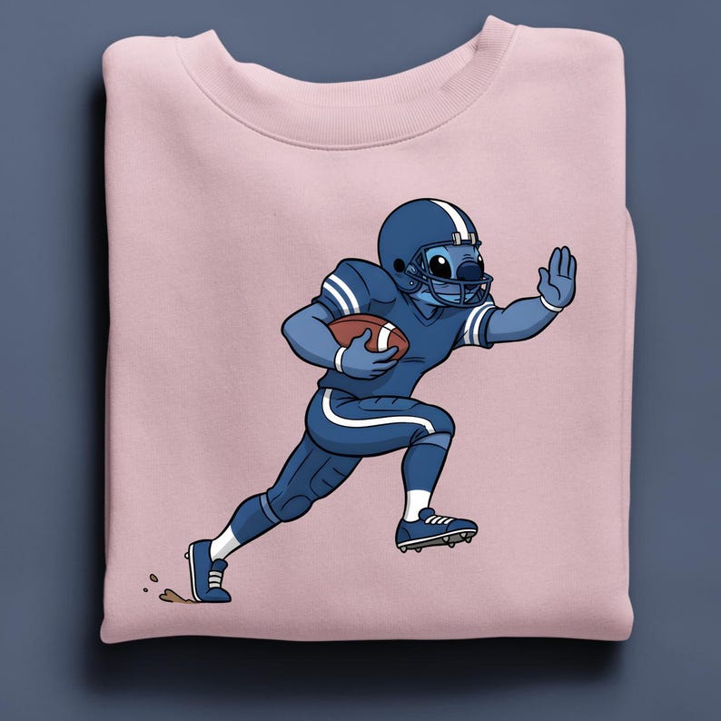 May include: A pale pink sweatshirt with a cartoon character in a blue American football uniform, running with a brown football. The character is wearing a helmet and has a hand raised. The design is centered on the sweatshirt.