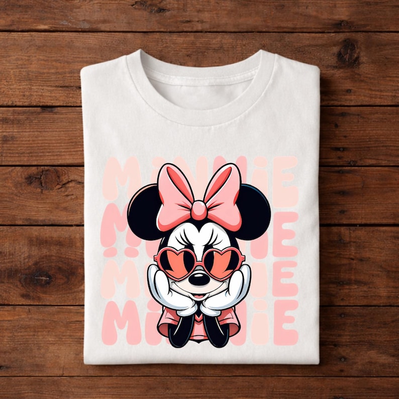 K&ouml;nnte beinhalten: Wei&szlig;es T-Shirt mit einem Cartoon-Design von Minnie Mouse. Minnie tr&auml;gt herzf&ouml;rmige Sonnenbrillen und eine rosa Schleife. Das Wort "MINNIE" ist vertikal in Rosa auf das T-Shirt gedruckt.