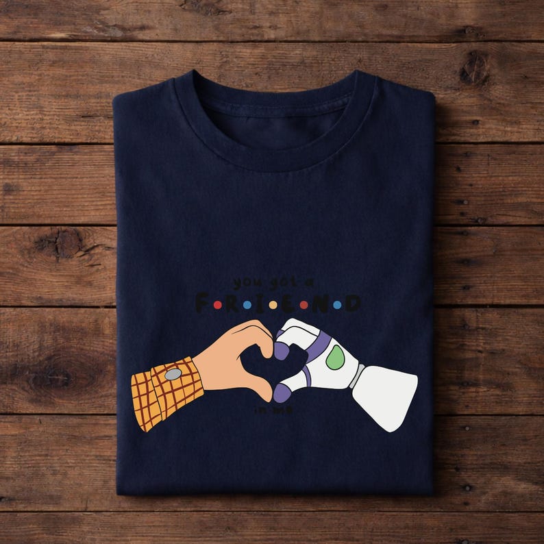 May include: Navy blue t-shirt featuring a heart made of cartoon hands, one with a plaid sleeve and the other a white and purple robotic arm. The text "You got a friend in me" is above the hands in a colorful font.