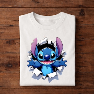 May include: White t-shirt featuring a cartoon illustration of Stitch, a blue alien character, bursting through a torn hole. Stitch has large ears, a wide smile, and outstretched arms. The design is centered on the shirt.