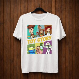 K&ouml;nnte beinhalten: Wei&szlig;es T-Shirt mit einer farbenfrohen Grafik von Charakteren aus dem Animationsfilm "Toy Story". Das Design umfasst Woody, Buzz Lightyear und andere Charaktere, mit den Worten "Toy Story" in Gelb.