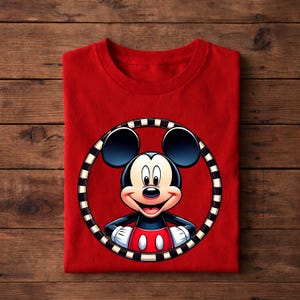 May include: A folded red t-shirt featuring a cartoon image of Mickey Mouse inside a black and white striped circle. Mickey Mouse is depicted with black ears, a black body, red shorts, and white gloves. The shirt is made of a soft material.