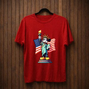 May include: Red t-shirt featuring a graphic of Mickey Mouse dressed as the Statue of Liberty, holding a torch and a tablet, with an American flag in the background. The design is colorful and patriotic.