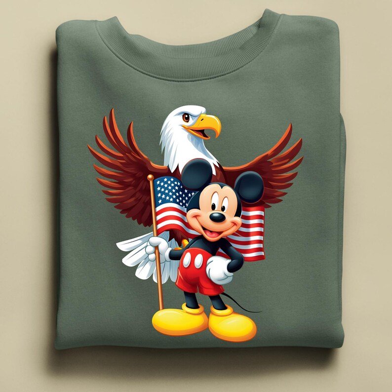 May include: A sage green sweatshirt featuring a graphic of Mickey Mouse holding an American flag, with a bald eagle behind him. Mickey is wearing red shorts, black gloves, and yellow shoes. The eagle has brown wings and a white head.