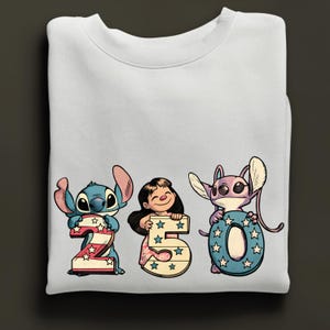 Puede incluir: Sudadera blanca con los personajes de dibujos animados Stitch, Lilo y Angel. Sostienen los n&uacute;meros 2, 5 y 0, decorados con estrellas y rayas. Los personajes son de estilo caricatura.