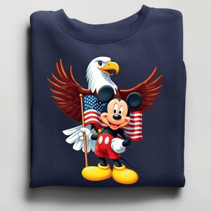 May include: Navy blue sweatshirt featuring a cartoon Mickey Mouse holding an American flag, with a bald eagle behind him. The eagle has brown wings and a white head. Mickey Mouse is wearing red shorts and yellow shoes.