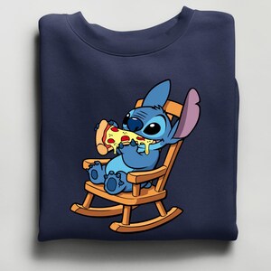 Pu&ograve; includere: Felpa blu navy con un'illustrazione a cartoni animati di Stitch di Lilo & Stitch. Stitch &egrave; raffigurato su una sedia a dondolo di legno, mentre mangia una fetta di pizza con formaggio fuso e pepperoni.