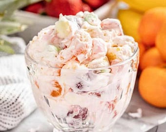 May include: A clear glass bowl filled with a colorful fruit salad. The salad includes a variety of fruits, such as strawberries, mandarin oranges, and marshmallows, mixed in a creamy sauce. The background features more fruit.