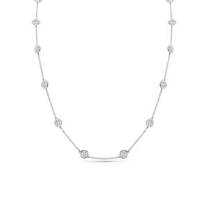 May include: A silver-toned chain necklace featuring evenly spaced, circular bezel-set clear stones. The delicate metal chain connects each individual stone setting, creating a continuous station necklace design with a polished, reflective finish.
