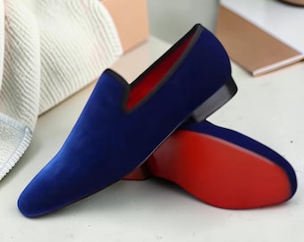 Pode incluir: Um par de mocassins de veludo azul royal com um design elegante de calçar e biqueira arredondada. O forro interior e toda a sola exterior são de uma cor vermelha sólida e vibrante, contrastando com o veludo azul profundo do cabedal.