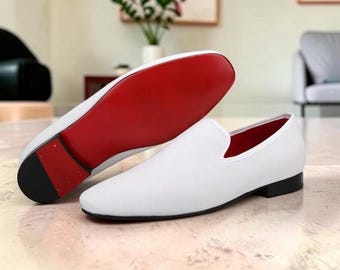 Pode incluir: Um par de mocassins brancos sem atacadores com uma parte superior branca lisa, uma sola vermelha vibrante, um forro interior vermelho e um salto baixo preto. Um sapato está posicionado para mostrar a sola vermelha, o outro está de lado.